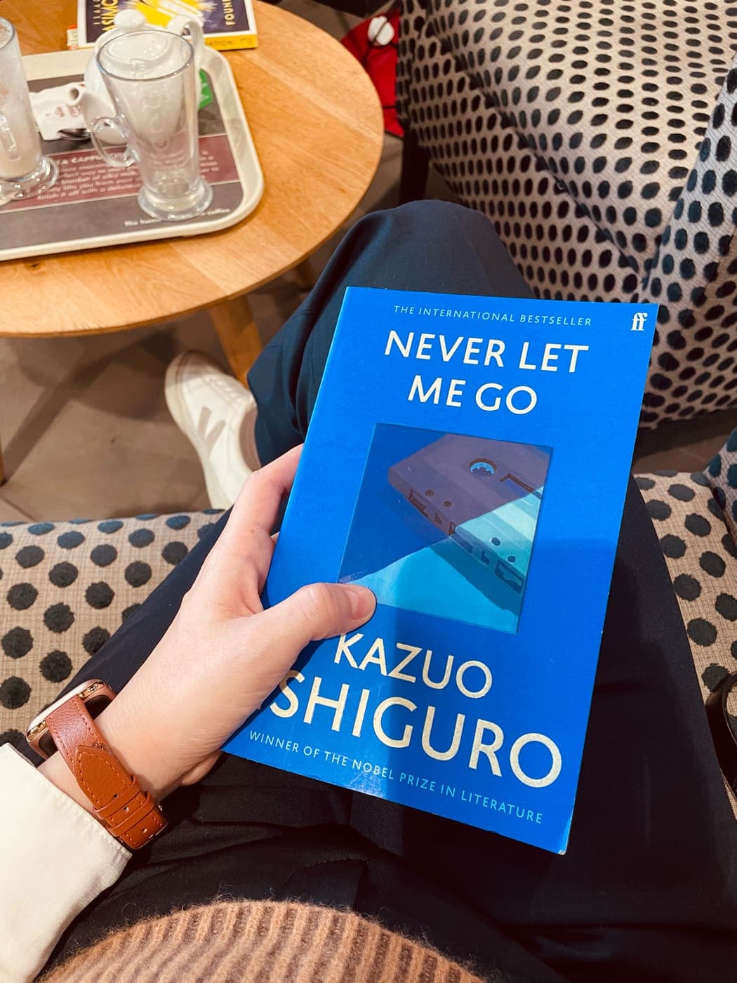Holding Kazuo Ishiguro's Never Let Me Go in a cafe armchair