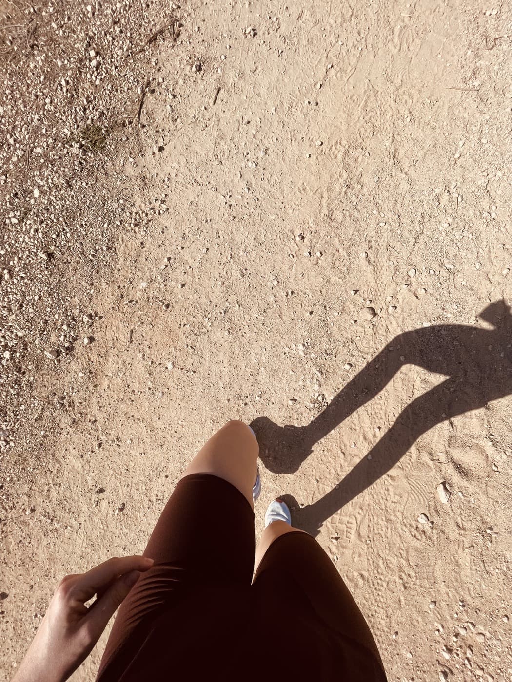 Looking down at my legs and long shadow partway through a run on a sunlit dirt trail